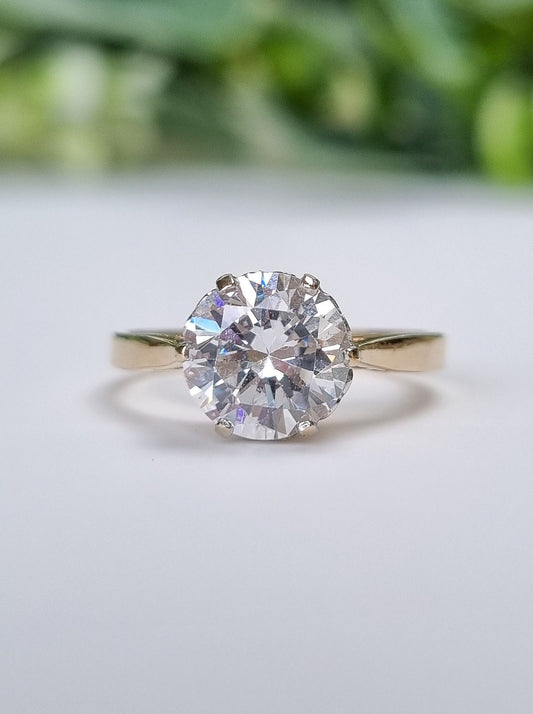 a vintage round brilliant cut cubic zirconia solitaire ring, with a solid 14ct yellow gold band. the stone measures 8mm across which is the equivalent to a 2ct diamond, and the setting holding the cubic zirconia features heart details.